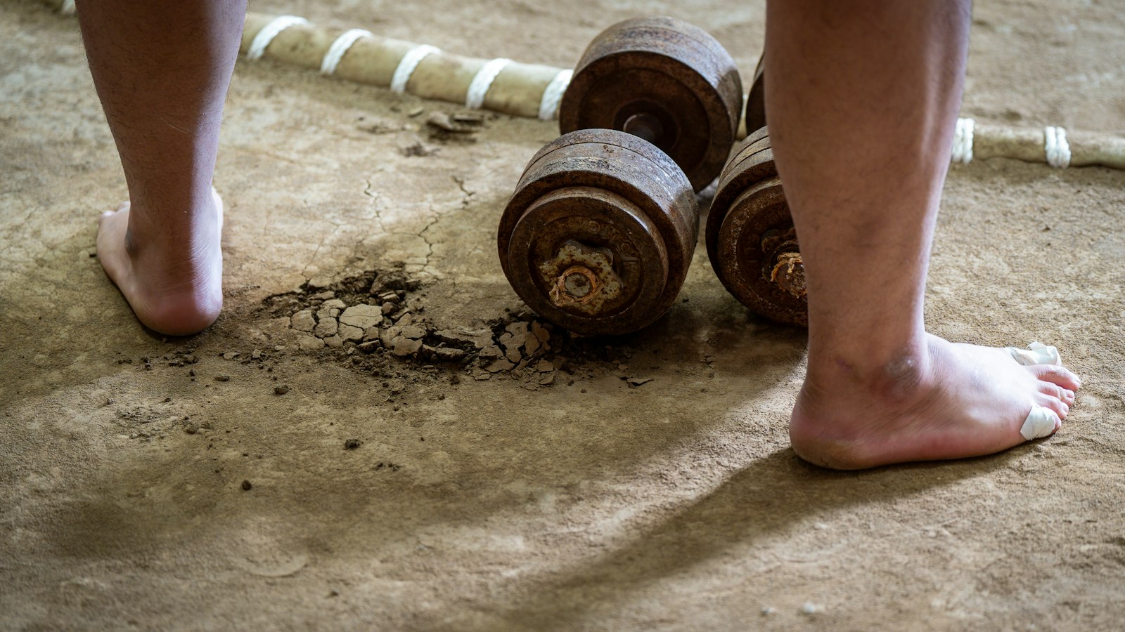 Bare feet near old weights on dirt ground