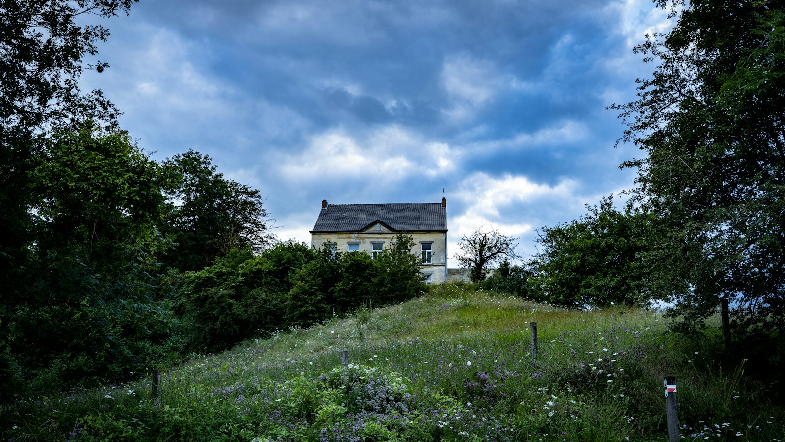 green grass field near brown concrete house under blue and white cloudy sky during daytime