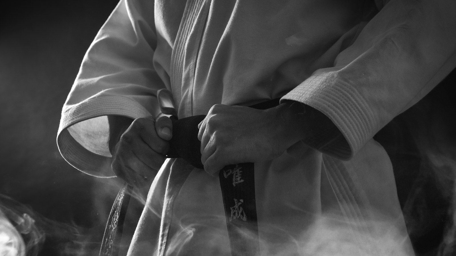 A person in a white martial arts gi tightening a black belt